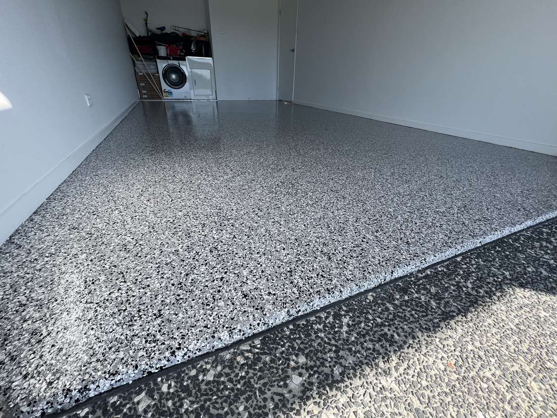 Grey and black flake epoxy garage floor meeting a coated driveway apron