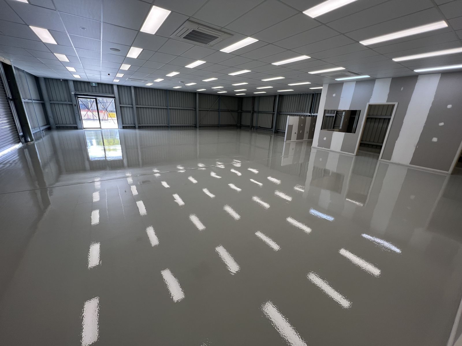 High-gloss grey epoxy floor through a large commercial shed with lights overhead